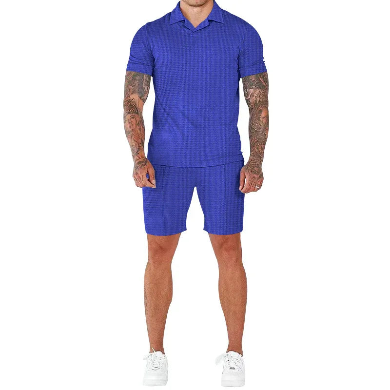 Man wearing a blue short-sleeve polo shirt and matching shorts with white sneakers, tattooed arms