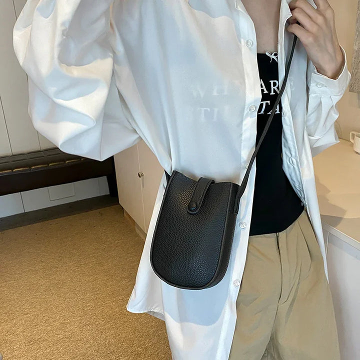 Person wearing white shirt and beige pants with a black leather crossbody bag indoors