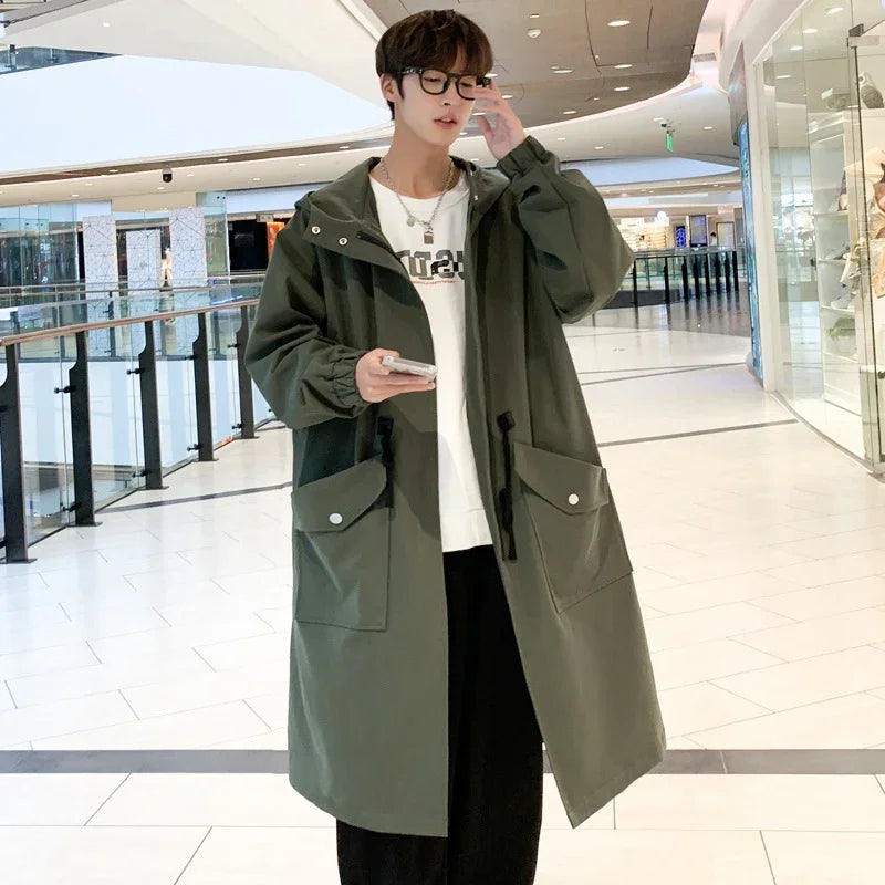 Young man in glasses wearing long olive green coat with large pockets in modern shopping mall