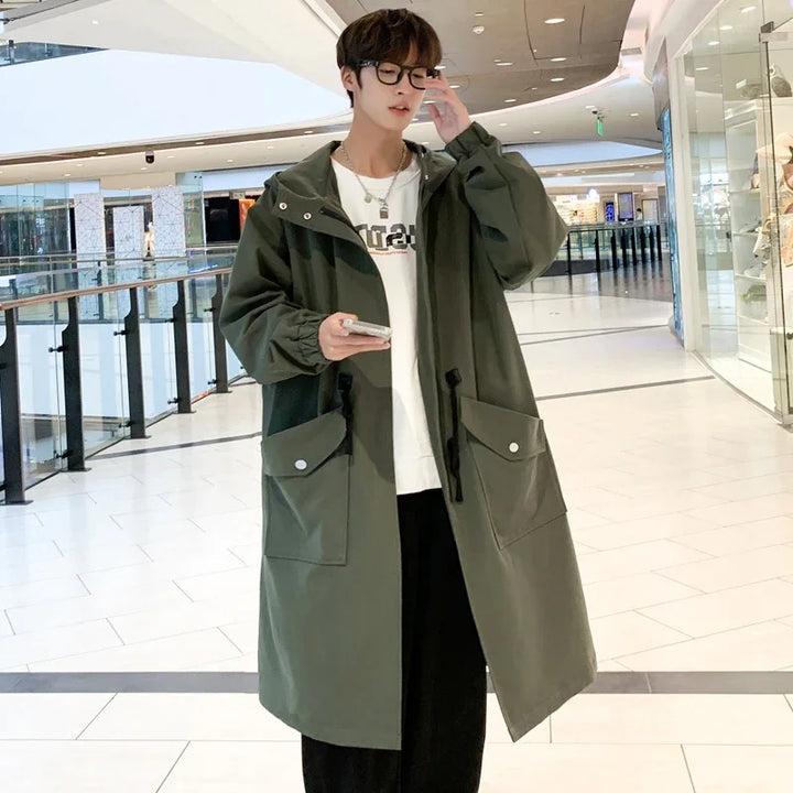 Young man in glasses wearing long olive green coat with large pockets in modern shopping mall