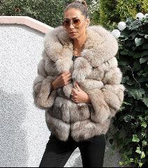 Woman wearing luxurious beige fur coat and sunglasses standing outdoors near green foliage