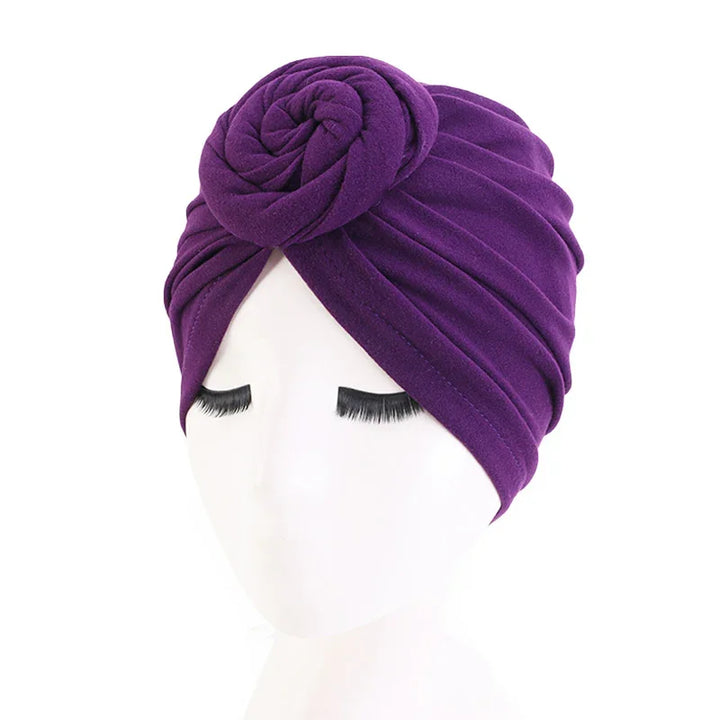 Purple turban headwrap with a twisted flower design on a white mannequin head