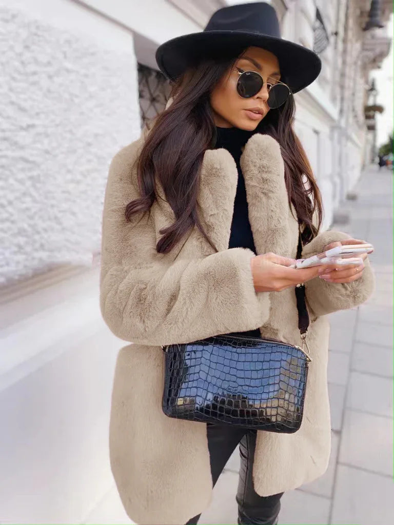 Woman in beige faux fur coat, black wide-brim hat, sunglasses, and black croc-embossed handbag using smartphone on city street