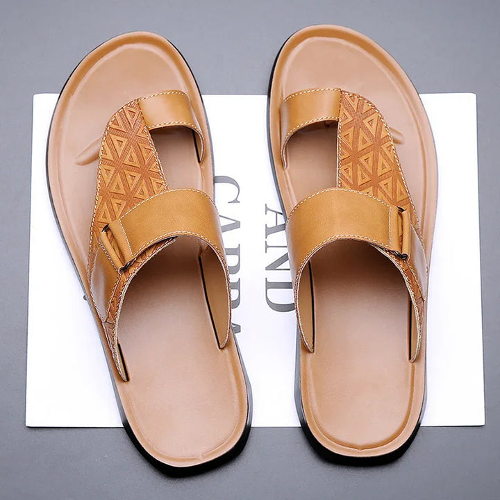 Men's tan leather slip-on sandals with geometric pattern and adjustable strap on gray background