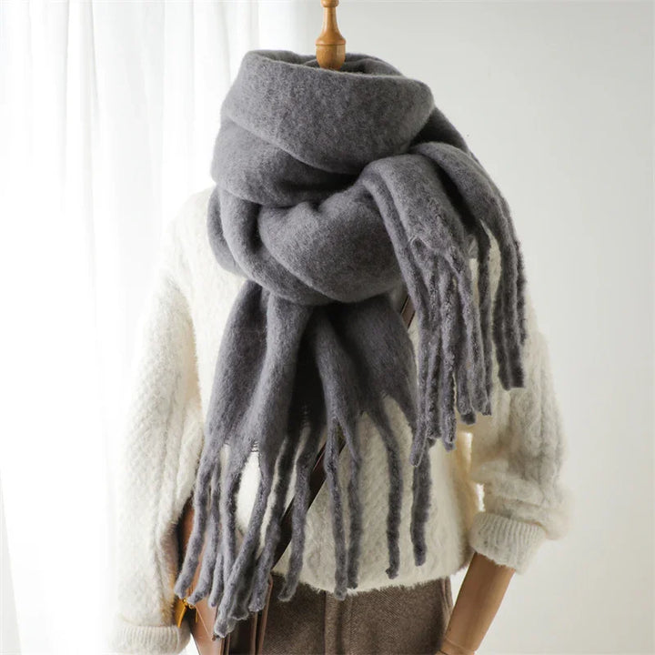 Cozy thick gray wool scarf with fringes on a mannequin wearing a white knit sweater