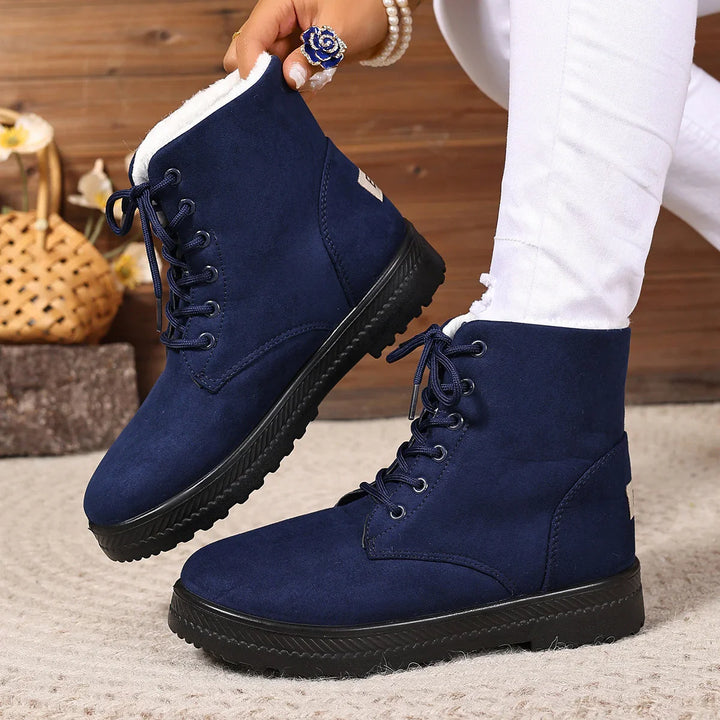 Women's navy blue fleece-lined winter boots with black soles and laces, worn with white pants