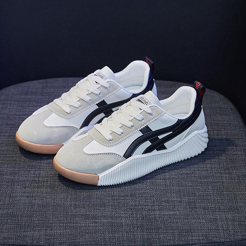 Pair of white and beige casual sneakers with black stripes and gum sole on gray fabric surface