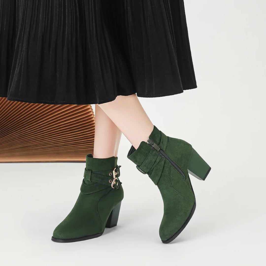 Woman wearing dark green suede ankle boots with buckles and block heels, paired with a black pleated skirt