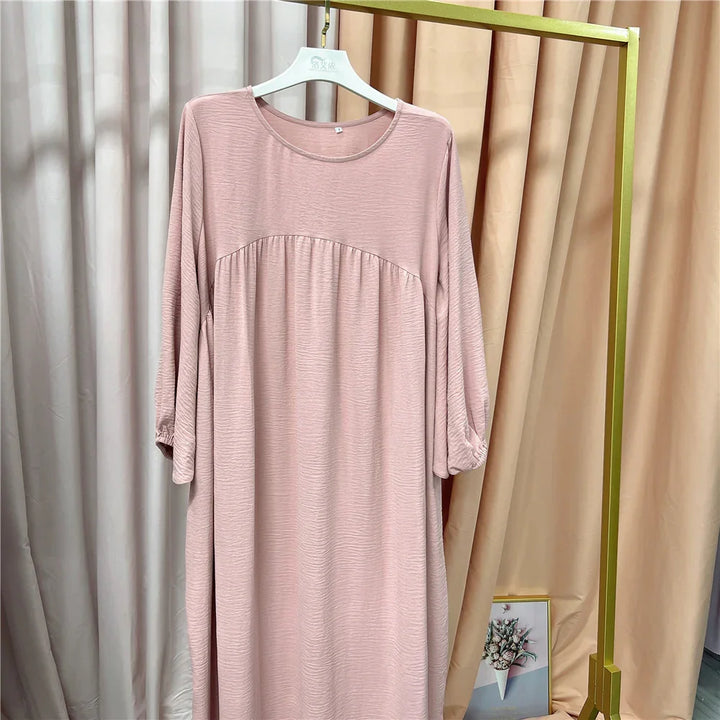 Light pink long-sleeve dress with textured fabric hanging on white hanger against beige curtain background