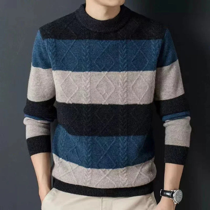 Man wearing a blue, black, and beige striped cable knit sweater with beige pants