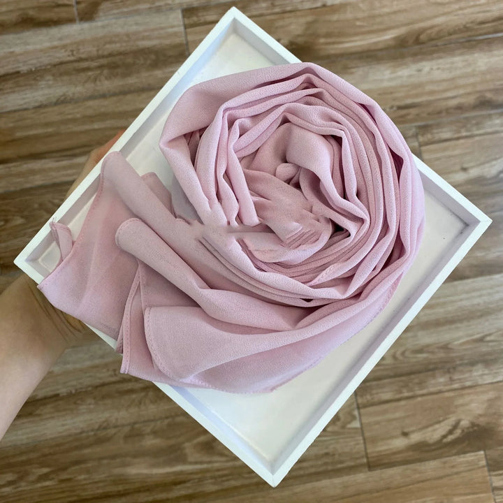 Hand holding white box with neatly folded soft pink chiffon fabric inside on wooden floor