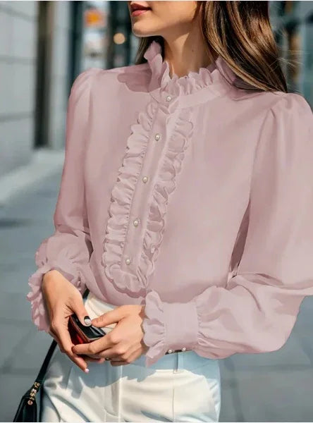 Woman wearing a light pink ruffled blouse with pearl buttons and puffed long sleeves, paired with white pants
