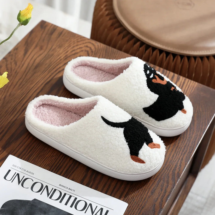 White fleece slippers with black and brown dog design on wooden table next to yellow flower and magazine