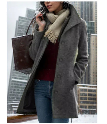 Woman in gray winter coat and beige scarf walking in snowy urban cityscape with tall buildings