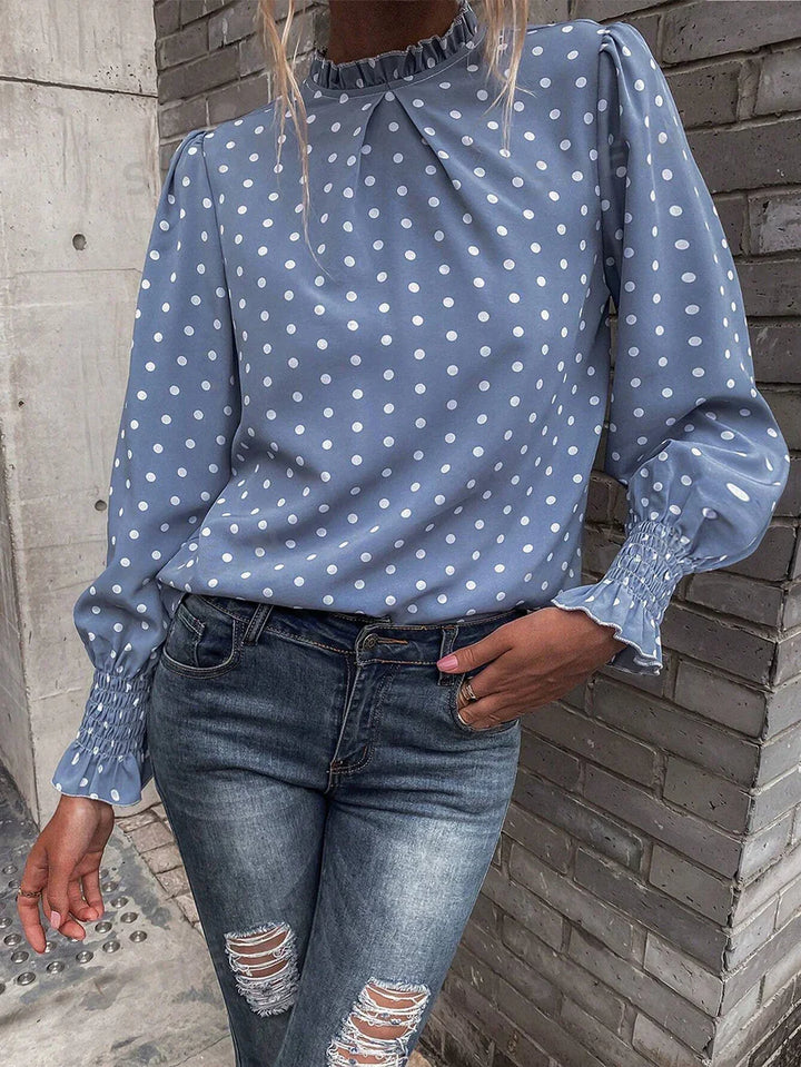 Woman wearing light blue polka dot blouse with smocked cuffs and ruffled collar paired with distressed jeans