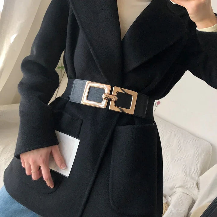 Black wool coat with wide lapel and stylish gold buckle belt worn over white top