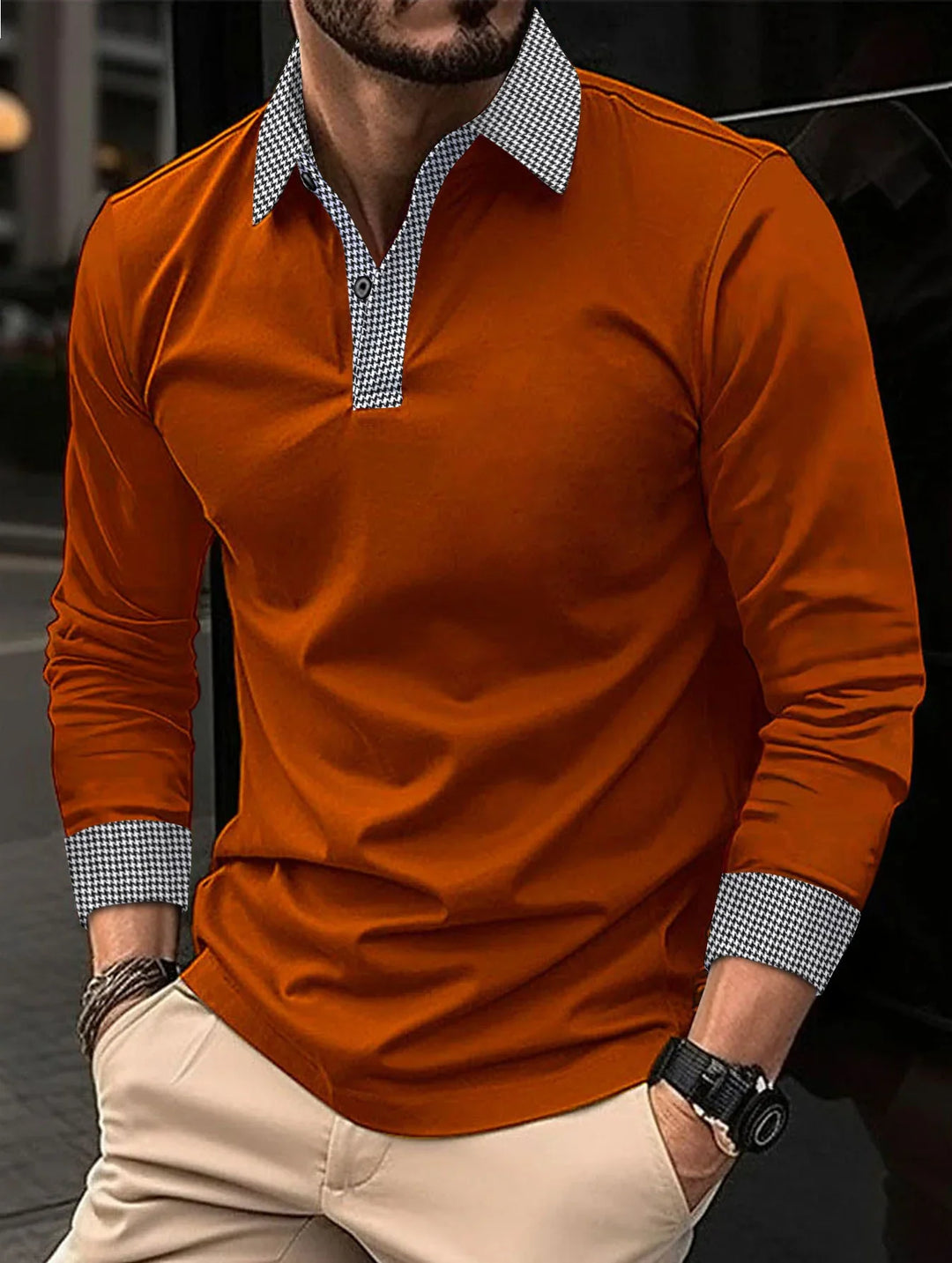Man wearing casual long sleeve orange shirt with black and white houndstooth collar and cuffs, beige pants