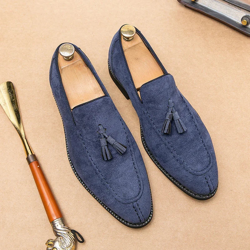 Blue suede tassel loafers with wooden shoe trees on tan surface next to a polished shoehorn