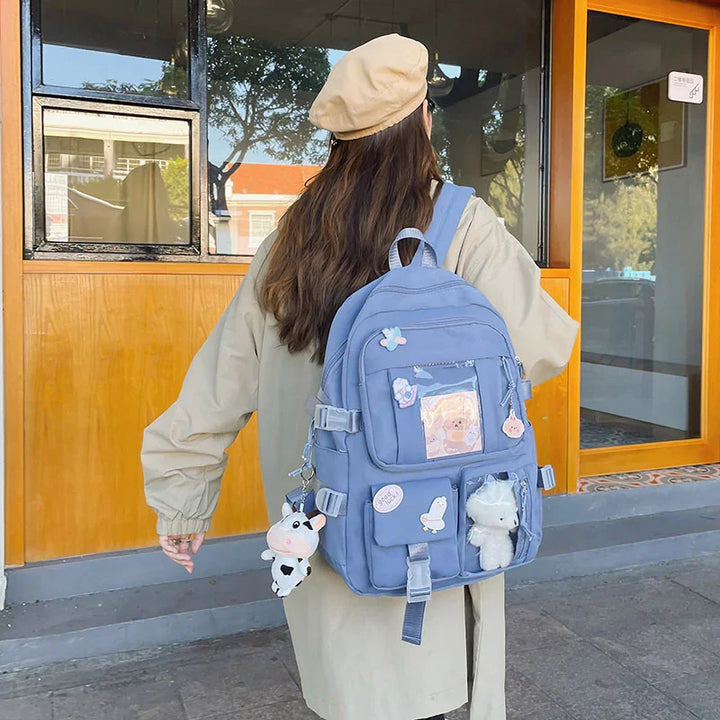 Woman wearing beige coat and beret carrying blue backpack with cute plush toy keychains outside a building