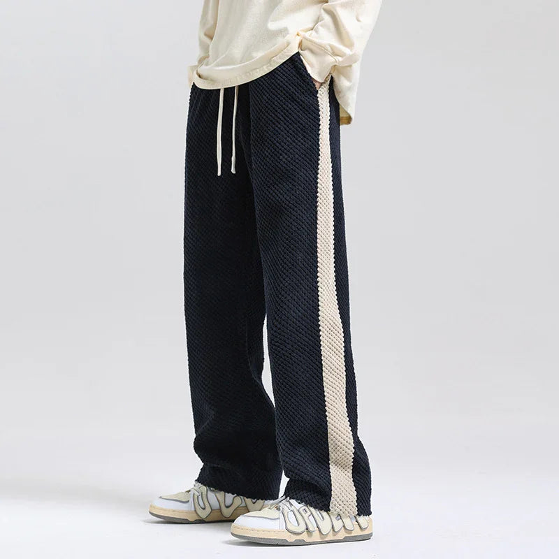 Black textured sweatpants with beige side stripe worn with white sneakers and cream long-sleeve top