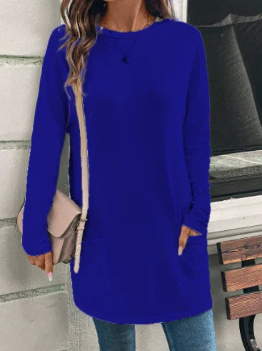 Woman wearing casual long sleeve royal blue tunic top with front pockets and light beige crossbody bag