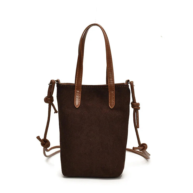 Small brown suede bucket bag with leather handles and adjustable shoulder strap on white background