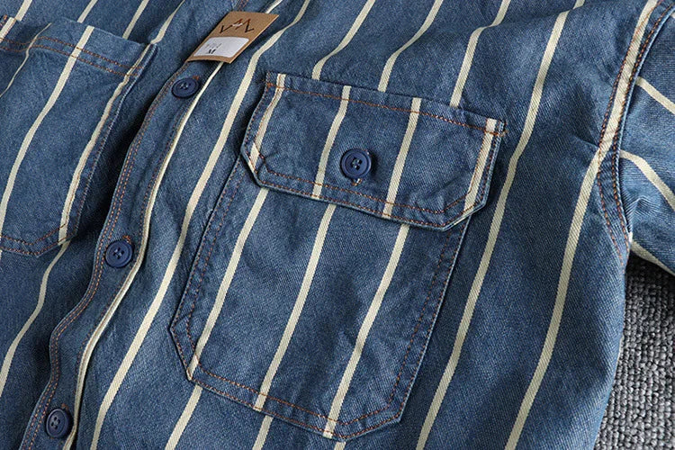 Close-up of blue denim shirt with white vertical stripes and front buttoned pockets on gray fabric