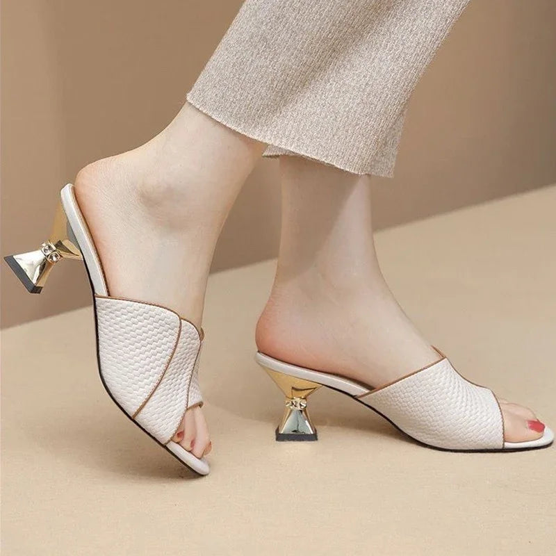 White woven open-toe mule heels with unique gold geometric block heels on feet