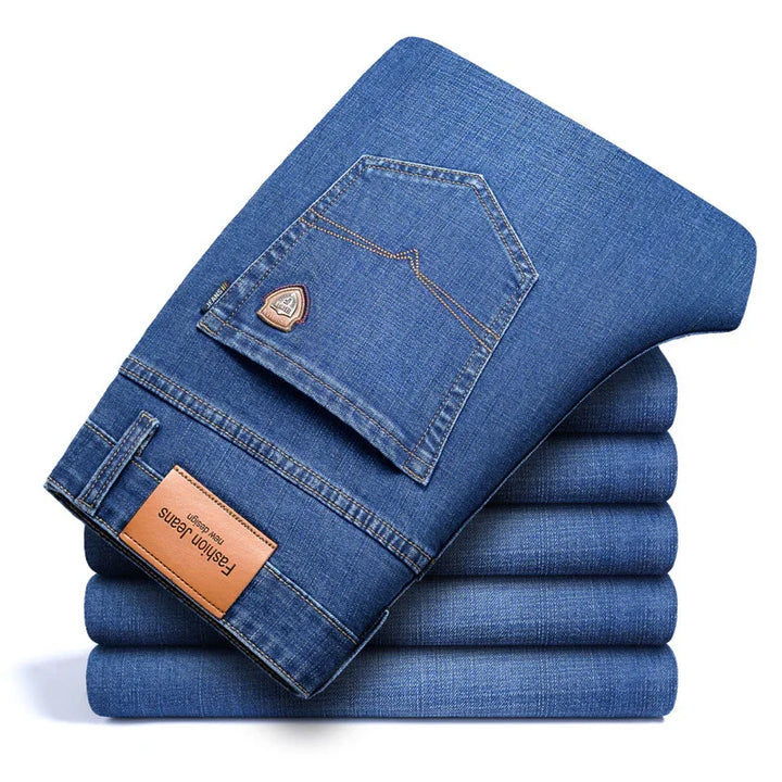 Stack of five blue denim jeans with folded pair on top showing back pocket and leather label