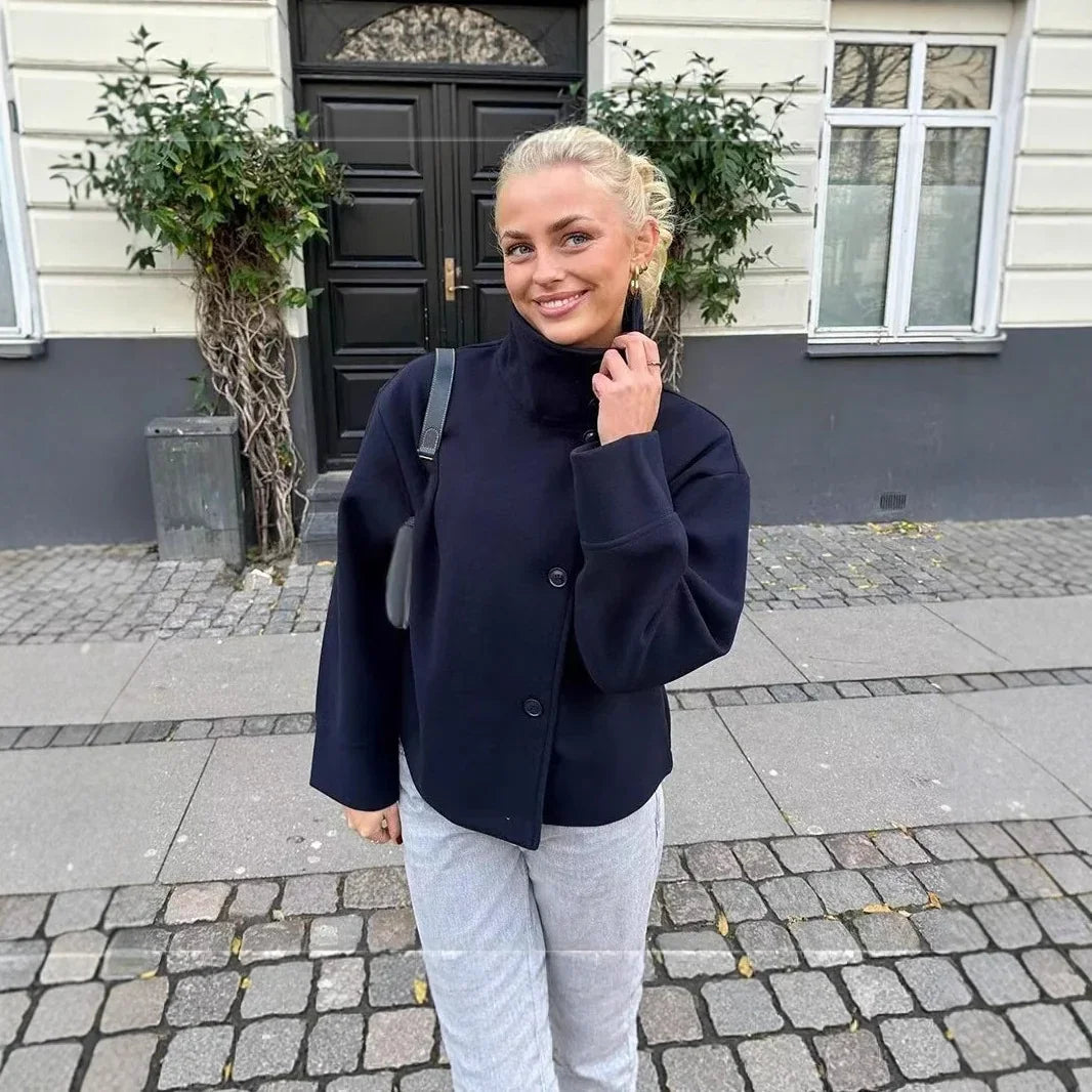 Smiling woman in black jacket and light pants standing on cobblestone street by building with black door