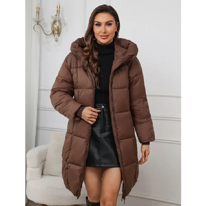 Woman wearing brown puffer coat with hood over black turtleneck and leather skirt in white room