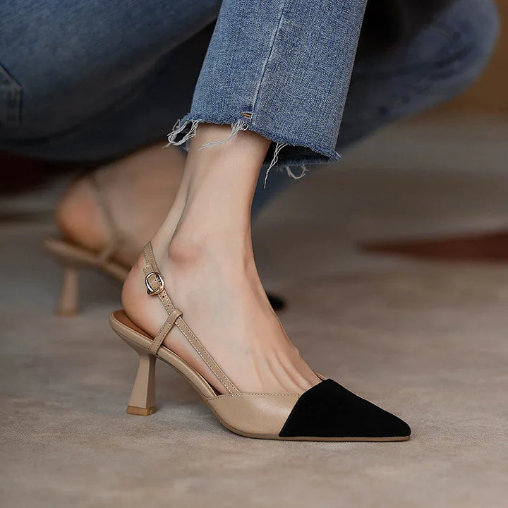 Beige and black pointed toe slingback high heel shoe worn with frayed hem blue jeans on carpet
