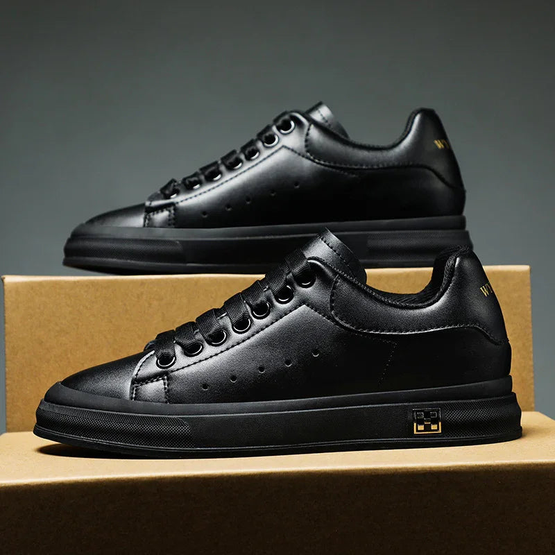 Pair of sleek black leather sneakers with black rubber soles displayed on brown cardboard boxes