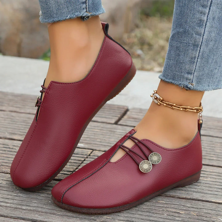 Close-up of feet wearing burgundy leather casual shoes with metal button details on wooden floor
