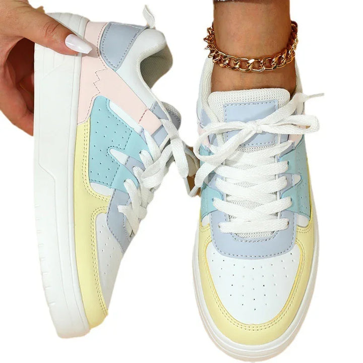 Colorful pastel sneakers with white laces, worn on foot and held by hand, featuring blue, yellow, pink accents