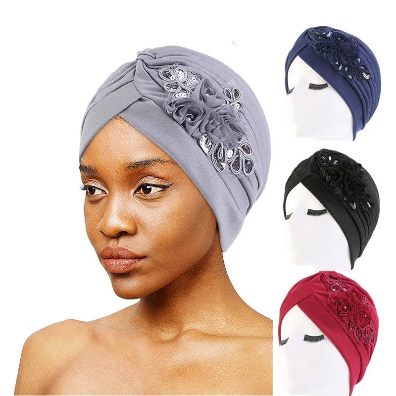 Woman wearing gray turban headwrap with floral and sequin embellishments, with navy, black, and red variants on mannequins