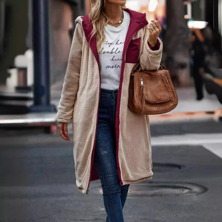 Woman wearing beige and burgundy sherpa fleece coat, white graphic tee, blue jeans, and carrying brown leather handbag