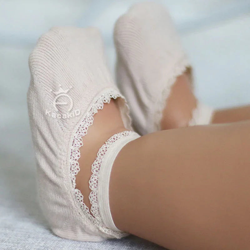 Close-up of feet wearing beige kids' ankle socks with lace trim on light background