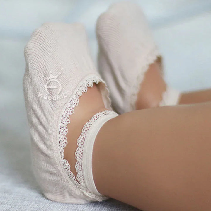 Close-up of feet wearing beige kids' ankle socks with lace trim on light background