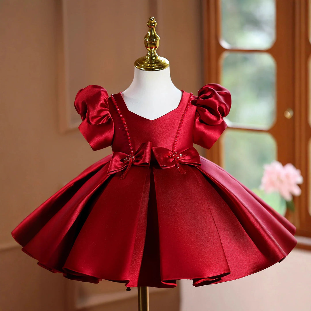 Elegant red satin baby dress with puff sleeves and bow details on mannequin in cozy room