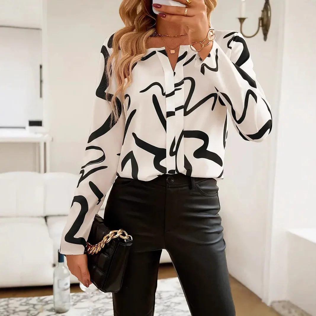 Woman wearing black and white abstract print blouse with black leather pants holding black purse