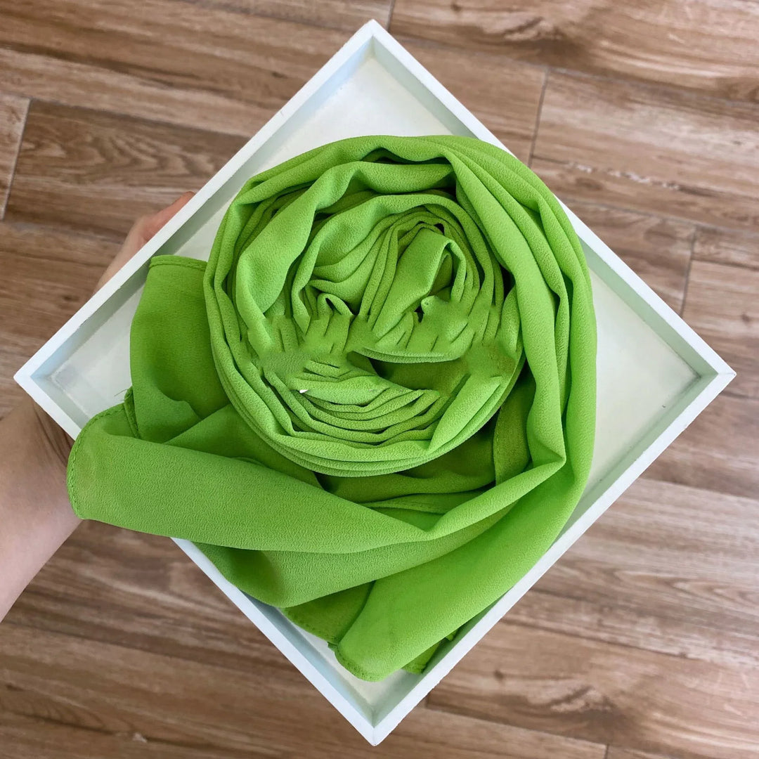 Hand holding white tray with rolled vibrant green fabric on wood floor background