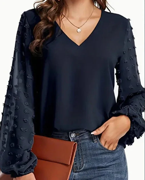 Woman wearing navy V-neck blouse with textured puff sleeves, paired with blue jeans and brown clutch