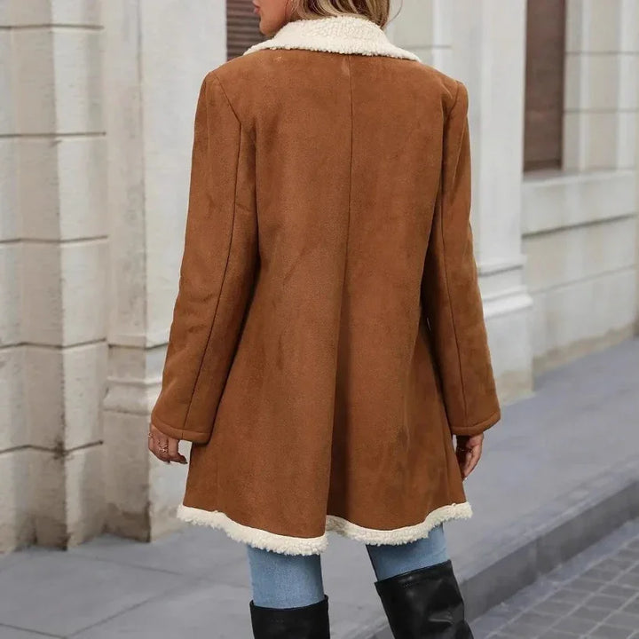 Woman wearing a brown faux suede coat with white sherpa lining on collar and hem, standing on city street