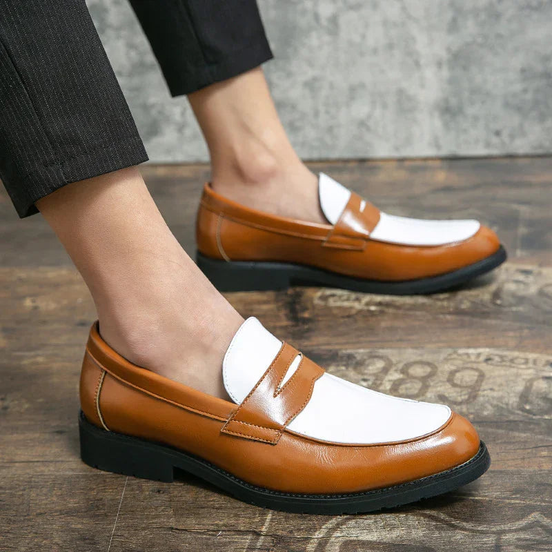 Men's two-tone brown and white leather slip-on loafers worn with black pants on wooden floor