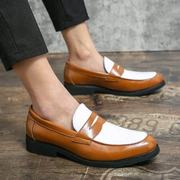 Men's two-tone brown and white leather slip-on loafers worn with black pants on wooden floor