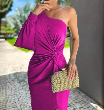 Woman wearing a stylish one-shoulder fuchsia dress with a knot detail, holding a gold clutch bag outdoors