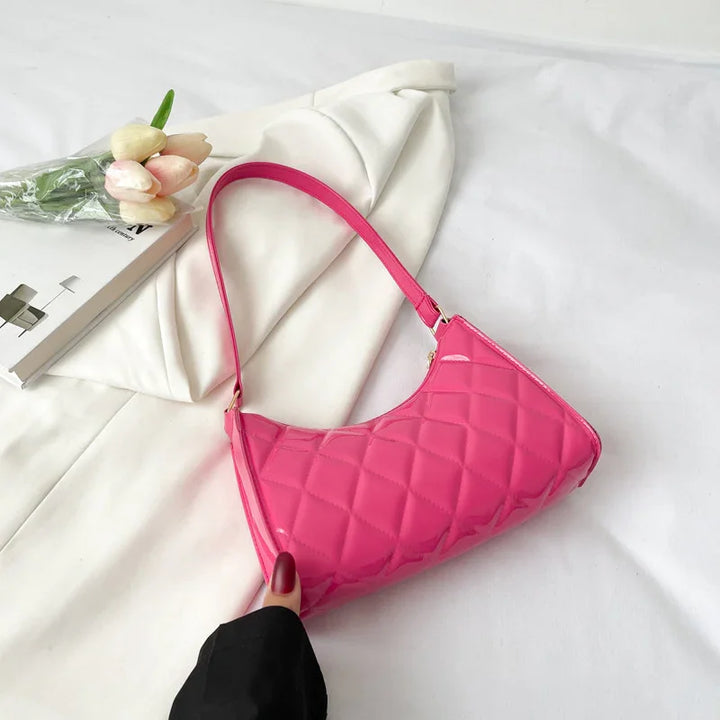 Pink quilted patent leather shoulder bag on white fabric with tulips and book nearby