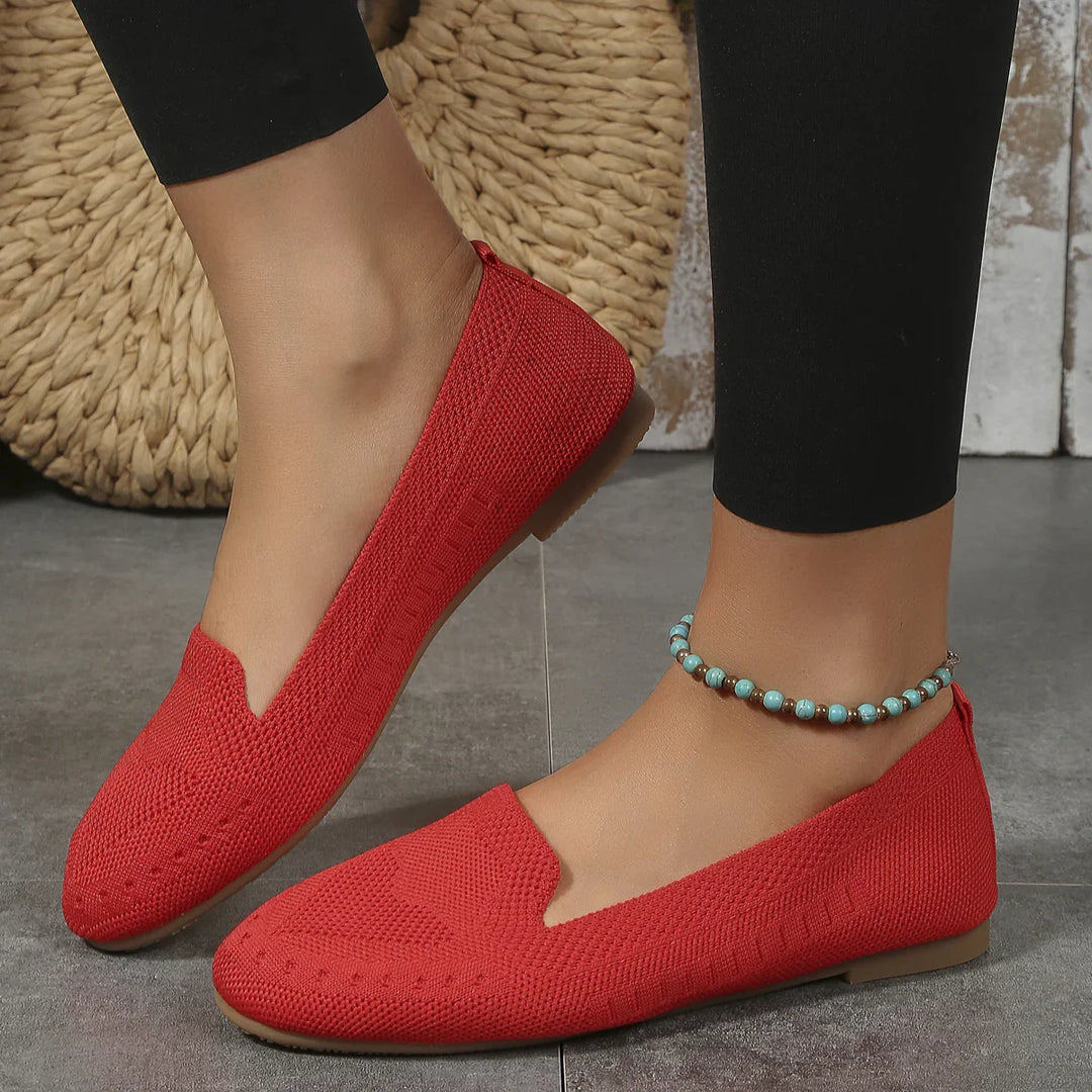 Red knitted flat shoes worn with black leggings and turquoise beaded anklet on tiled floor