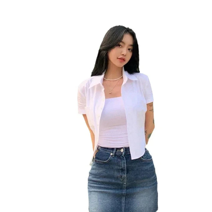 Young woman wearing white short-sleeve shirt over white tank top with denim skirt, casual outfit